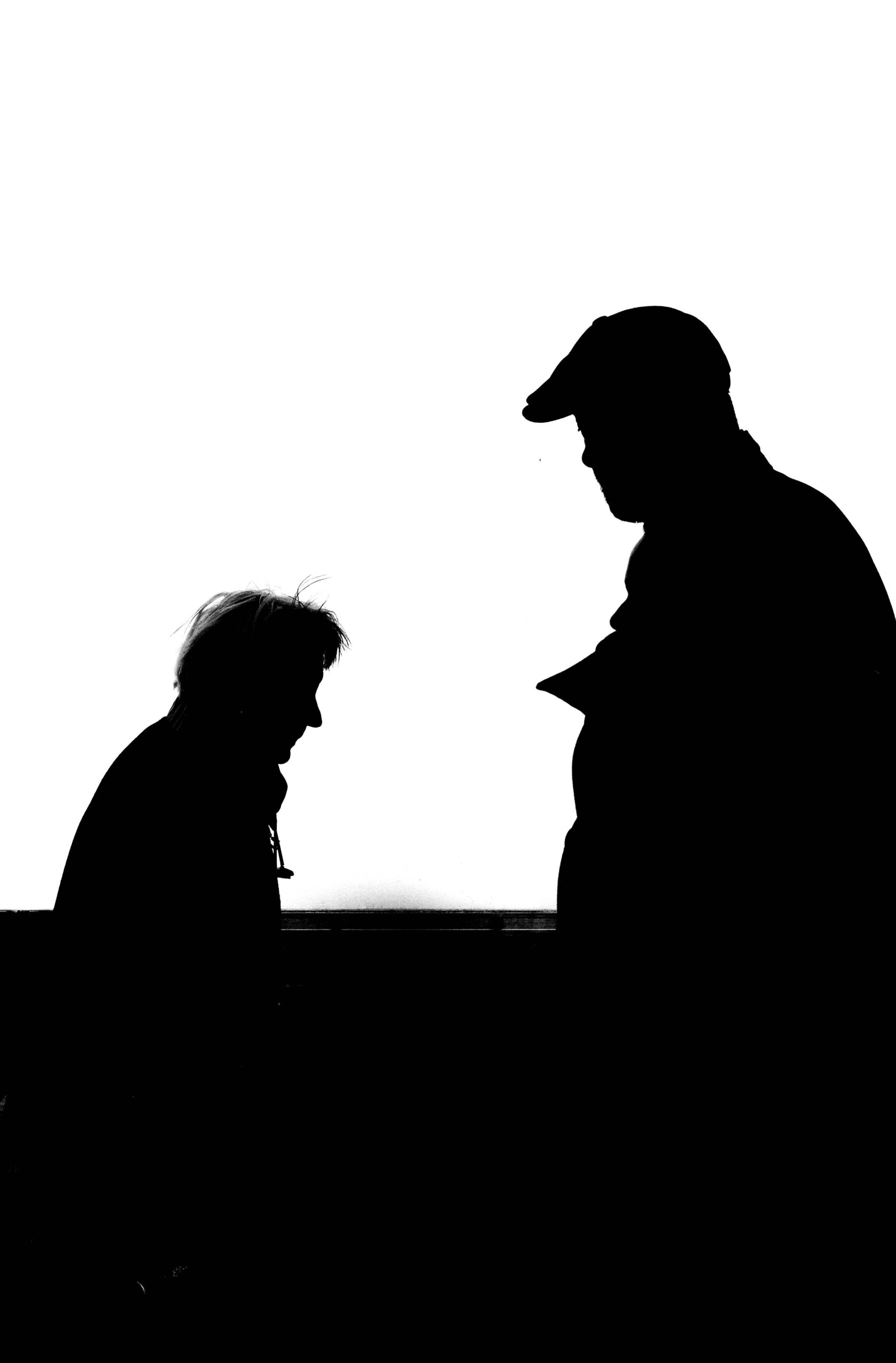 High contrast silhouette photo capturing two adults conversing against a white background.